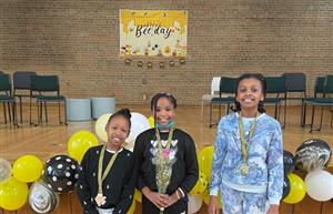  Three students with spelling bee medals on a school stage